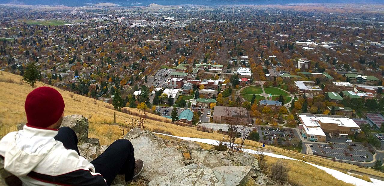 Student sitting on a hill overlooking school campus